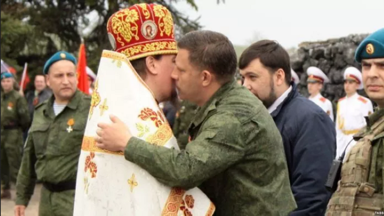 A UOC MP priest kisses the then leader of Russia's proxy "DNR" in eastern Ukraine, Aleksander Zakharchenko (center), with one of the leaders of the same group, Denis Pushilin, wanted in Ukraine and under international sanctions, behind him. Savur-Mohyla, Donetsk Oblast, 8 May 2015.  - фото 1